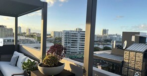 Un balcón con un sofá blanco, una planta en maceta y vistas a un paisaje urbano con edificios y un puerto deportivo.
