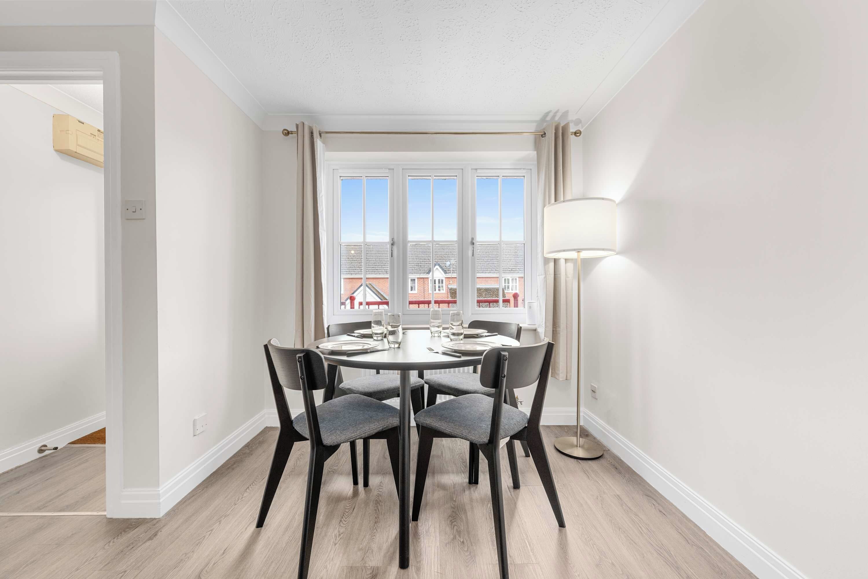 A dining area with a round table, four chairs, and a floor lamp.