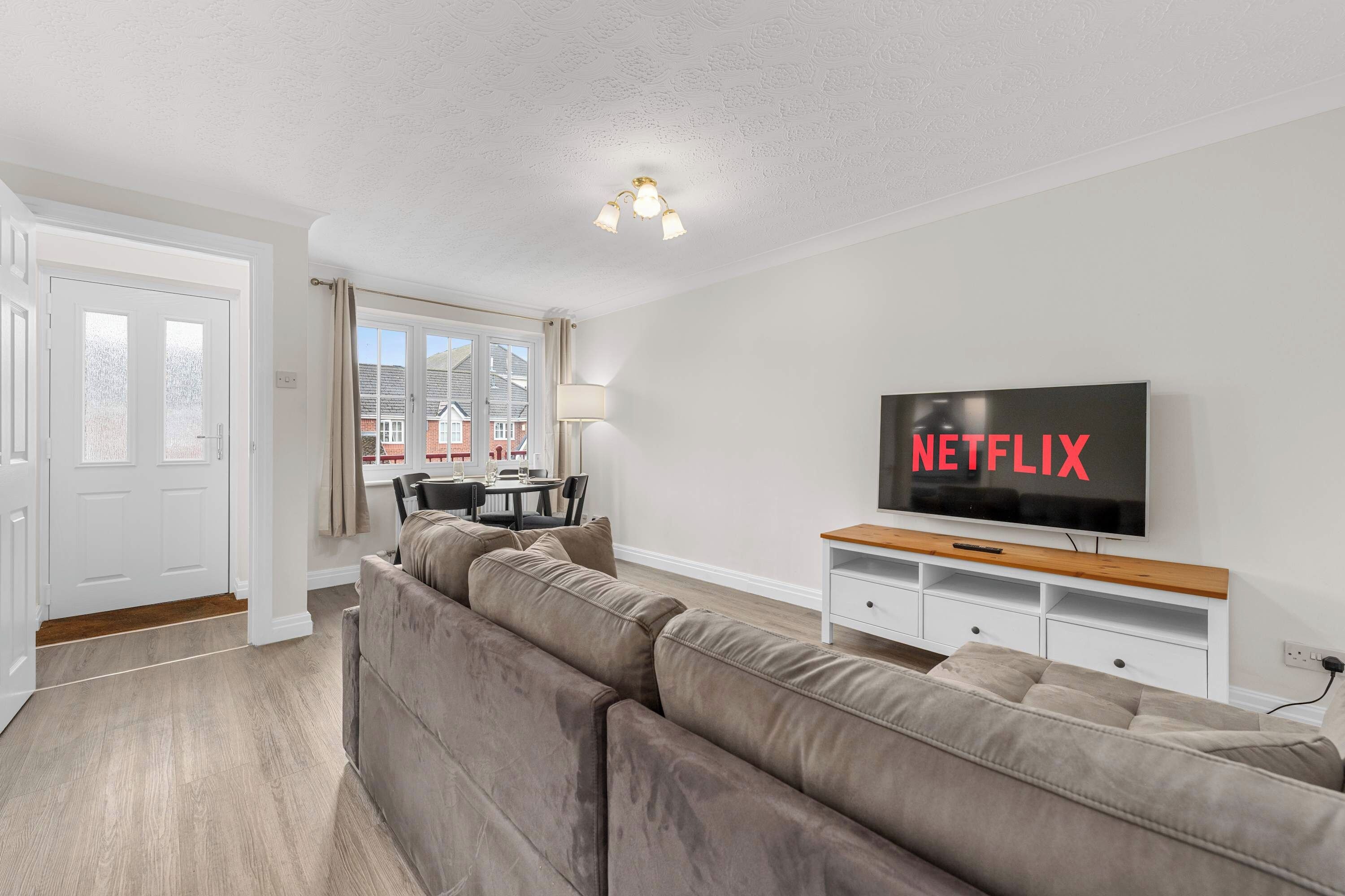 Sala de estar moderna com sofá seccional, área de jantar e televisão exibindo 'NETFLIX'.