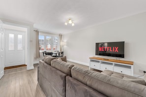 Sala de estar moderna com sofá seccional, área de jantar e televisão exibindo 'NETFLIX'.