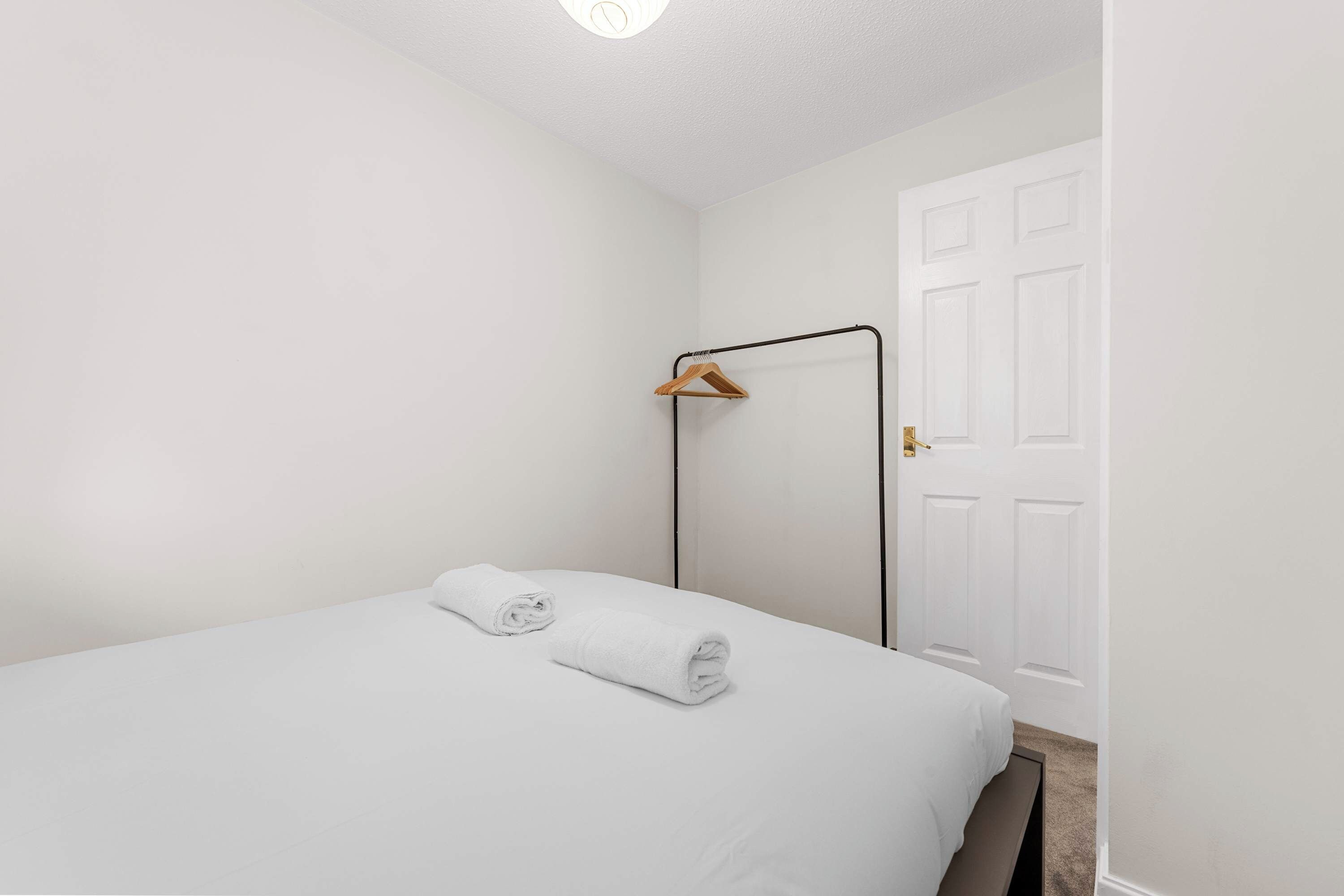 Uma cama de solteiro com duas toalhas enroladas, um cabide de metal e uma porta branca.