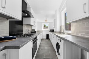 Une cuisine moderne avec des meubles blancs, une hotte en acier inoxydable et un lave-linge encastré.