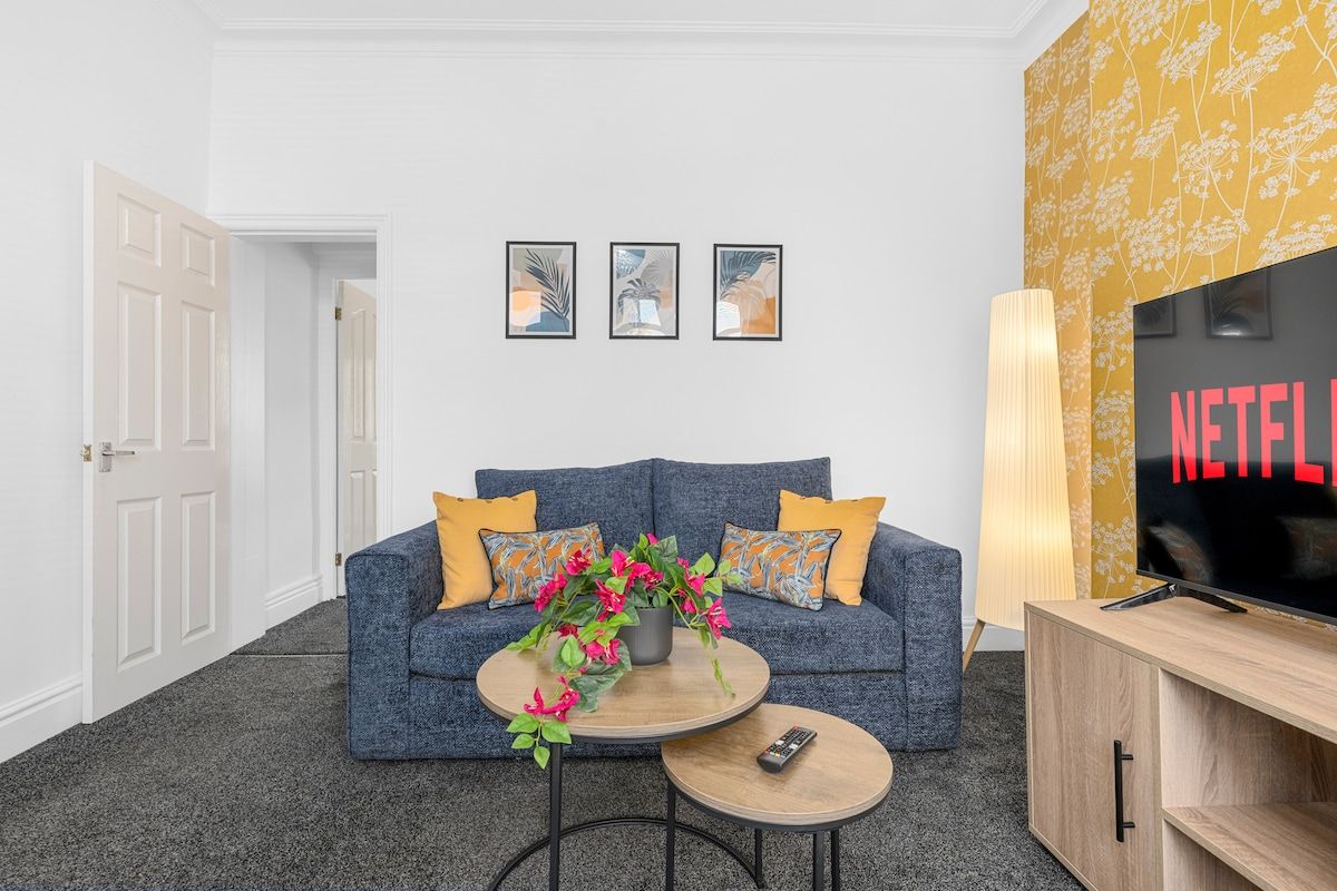 Un salon avec un canapé, une table basse et un téléviseur. Trois tableaux encadrés sont accrochés au mur.
