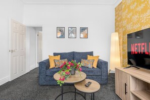 Un salon avec un canapé, une table basse et un téléviseur. Trois tableaux encadrés sont accrochés au mur.