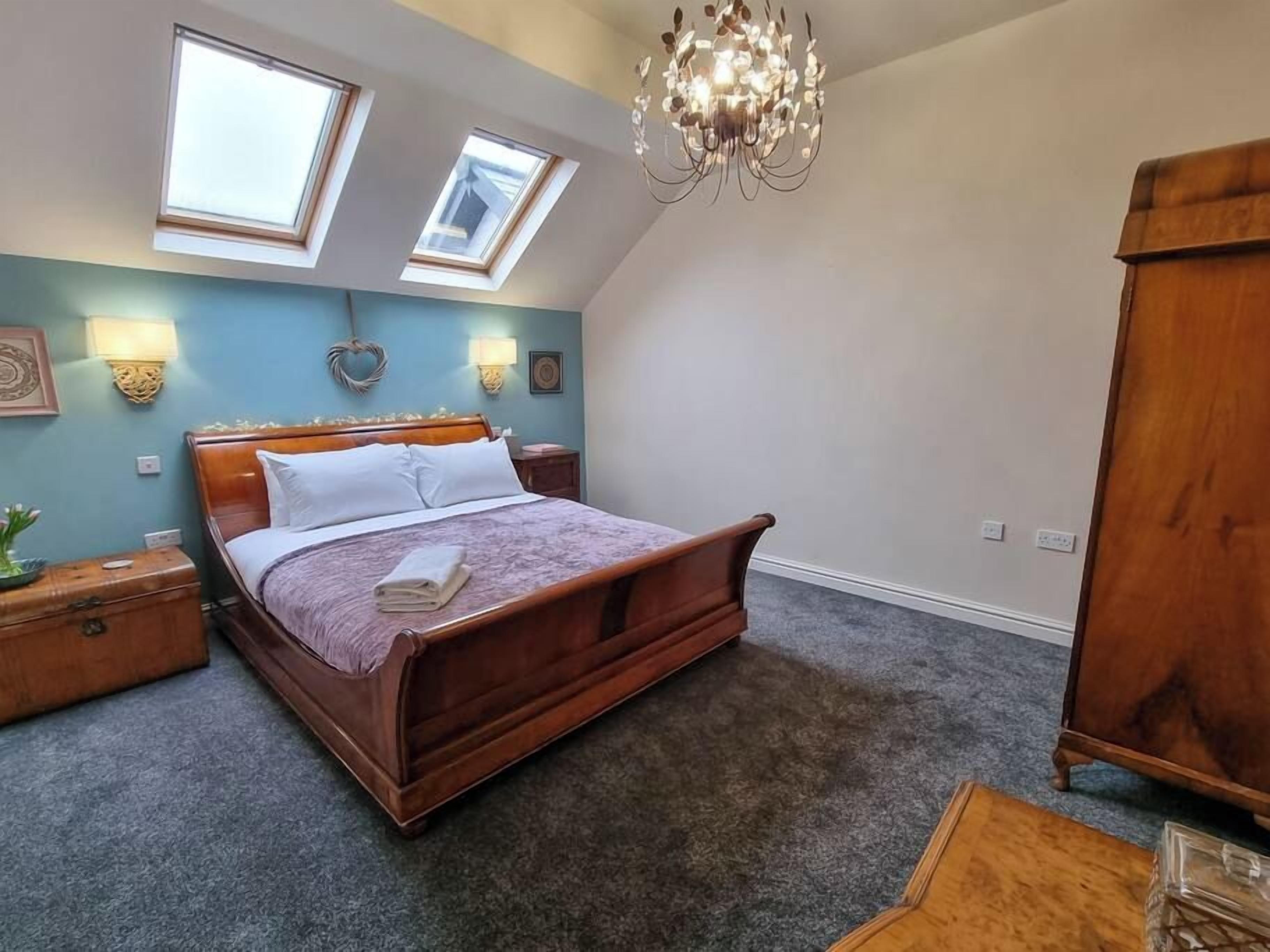 Quarto com cama de madeira, duas claraboias, um lustre e um guarda-roupa de madeira.