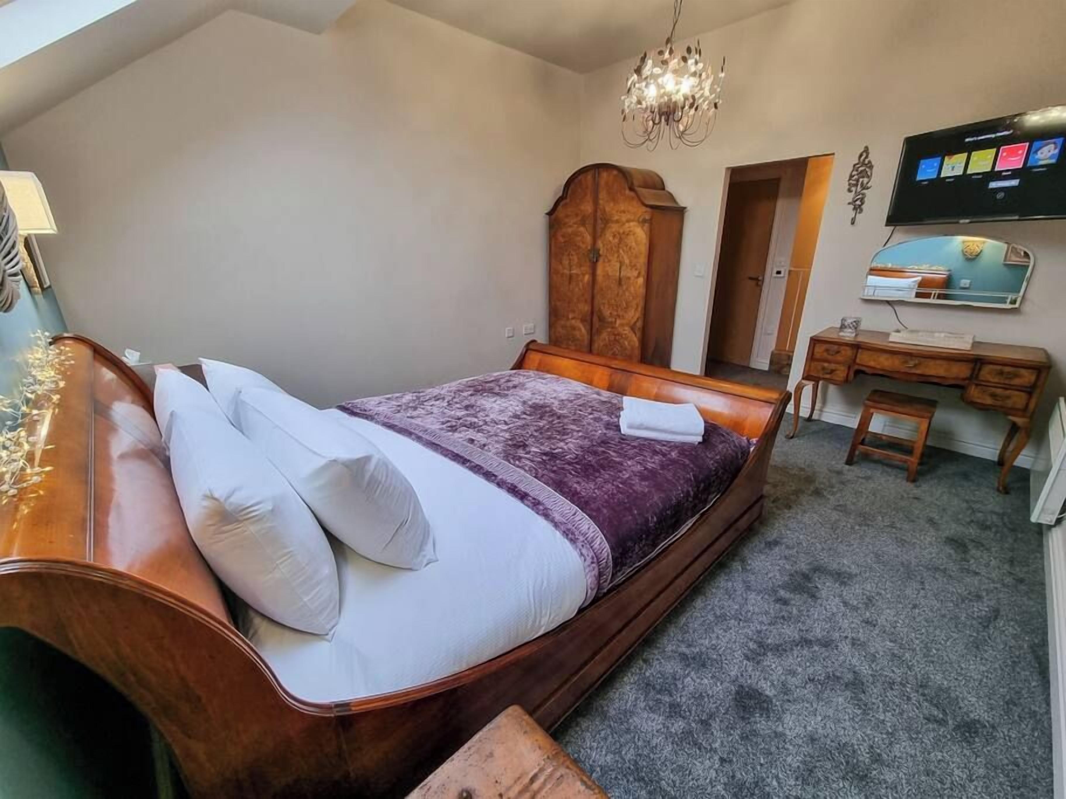 Een slaapkamer met een gebogen bed, een houten garderobe, een bureau en een televisie aan de muur.