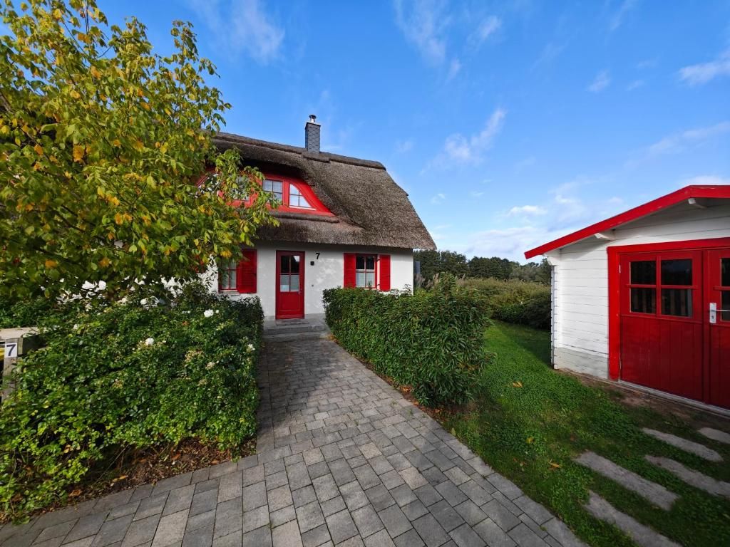 Ein Haus mit einem Strohdach, einer roten Tür und einem gepflasterten Weg, der davor führt.