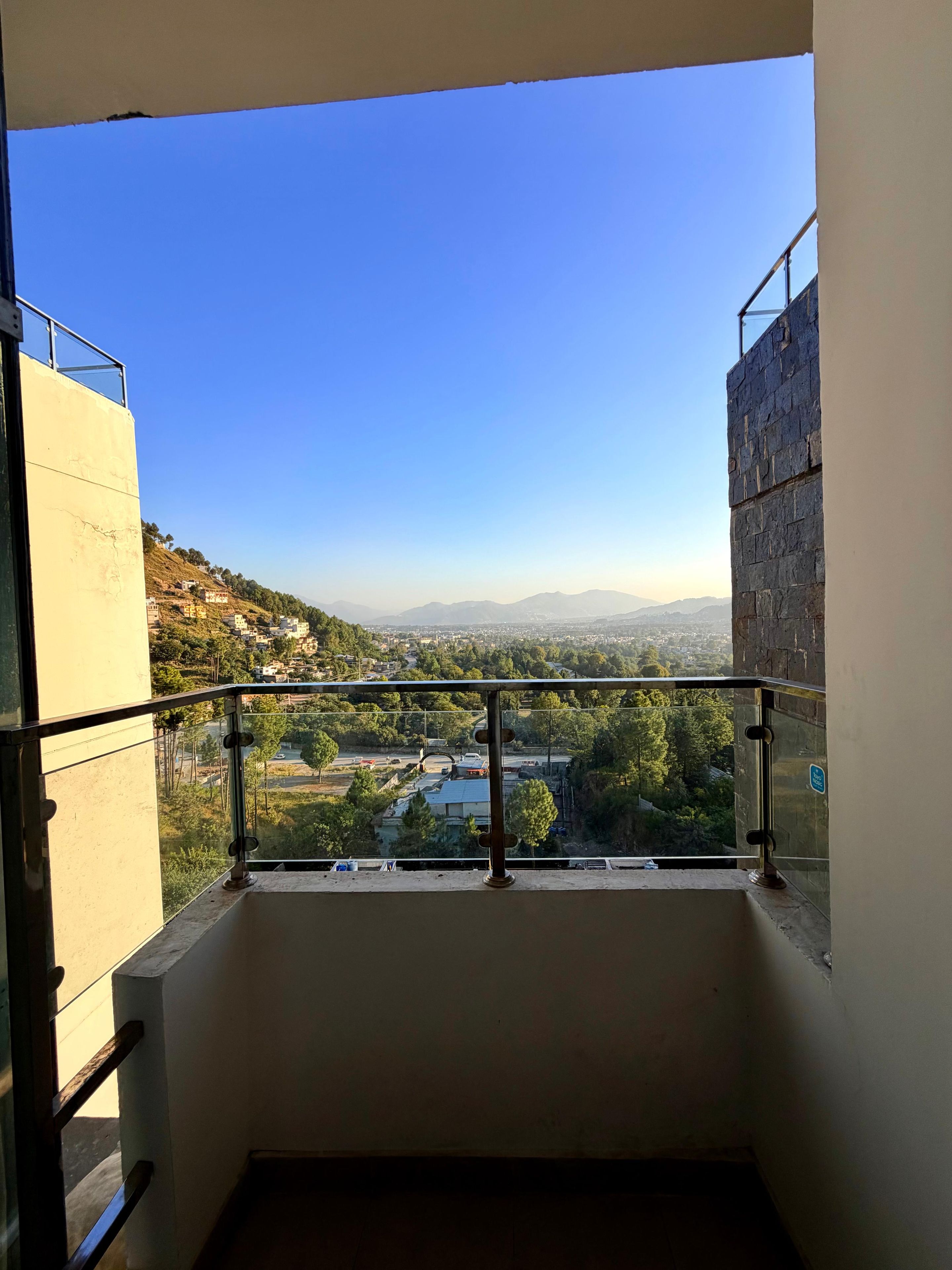 Ein Balkon mit freiem Blick auf eine Stadtlandschaft, einschließlich Gebäude und einer entfernten Bergkette.