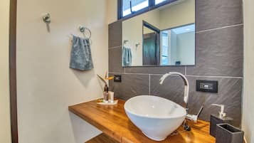 Un baño moderno con un lavamanos tipo lavabo, una encimera de madera, un espejo y un perchero para toallas.