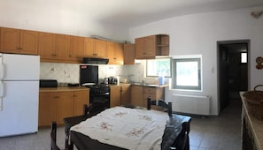 A kitchen with wooden cabinets, a refrigerator, a stove, and a window providing natural light. - Villa Gaia - Private Pool Villa in Monemvasia (Άγιος Στέφανος)