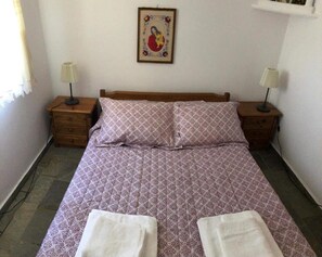 Un dormitori amb un llit, dues mesetes de nit, un quadre penjat a la paret i una finestra amb cortines.