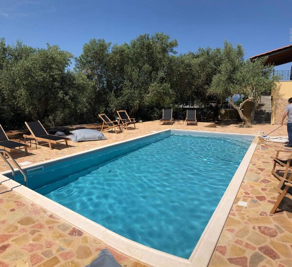 A rectangular swimming pool with clear blue water, surrounded by lounge chairs and a stone patio. - Villa Gaia - Private Pool Villa in Monemvasia (Άγιος Στέφανος)