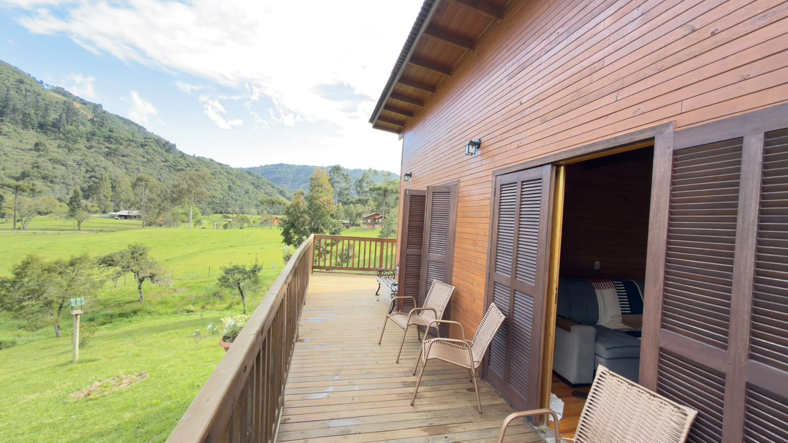 Una terraza de madera con muebles de exterior, con vistas a un paisaje verde con árboles y una colina.