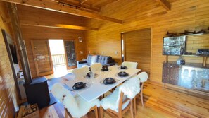 Interior de madera con una mesa de comedor para cuatro, un sofá y una zona de cocina con cristalería.