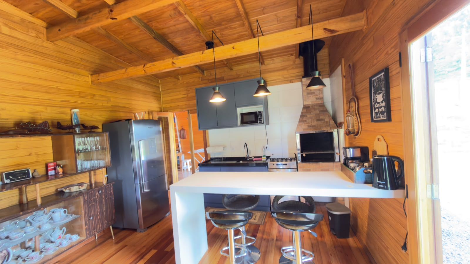 Interior de madera con una zona de cocina que incluye un refrigerador, horno y taburetes de bar.
