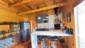 A wooden interior with a kitchen area featuring a refrigerator, oven, and bar stools. - Casa Blue Sunset (Urubici)
