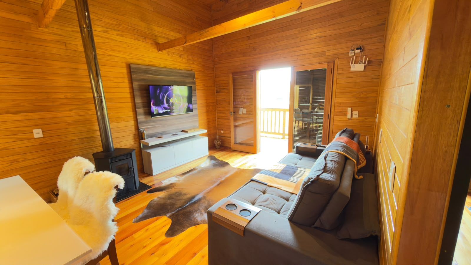 Interior de una cabaña de troncos con sofá, televisión y chimenea.