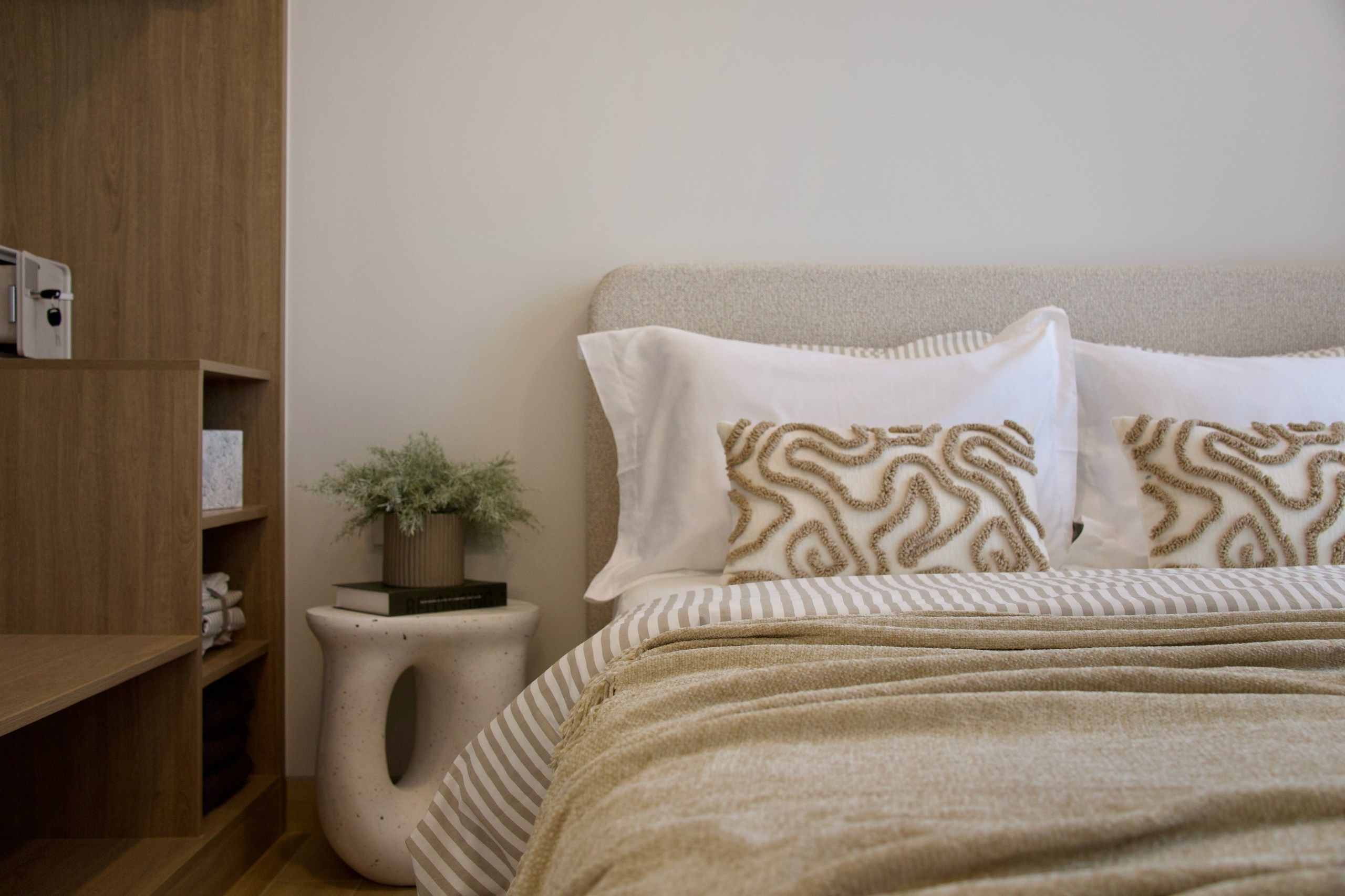 A bedroom with a bed, pillows, a bedside table with a plant, and a wooden shelf.
