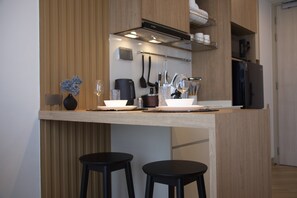 A modern kitchen with a wooden countertop, two black stools, and various kitchen utensils. - Mountain View Corner Unit in Laguna with Rooftop Pool & 10min-walk to the Beach (ตำบลเชิงทะเล)