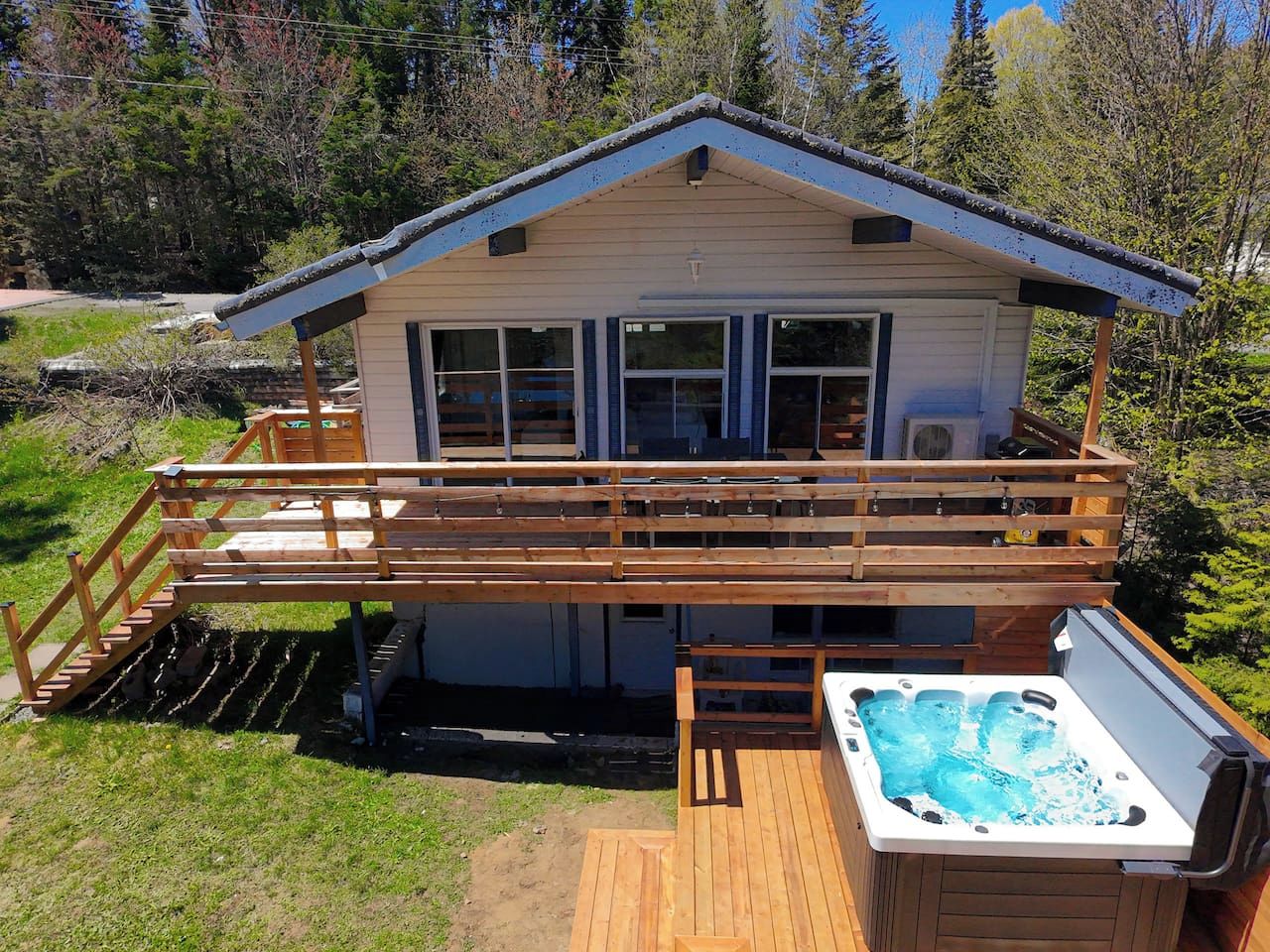 Una cabaña de dos pisos con terraza, jacuzzi y vista al bosque circundante.