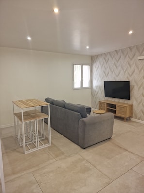 A modern living room with a sectional sofa, a TV on a wooden stand, and a small round table.