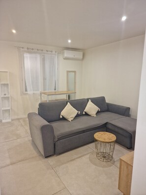 A modern living room with a grey sectional sofa, a small round coffee table, and a white air conditioning unit on the wall.