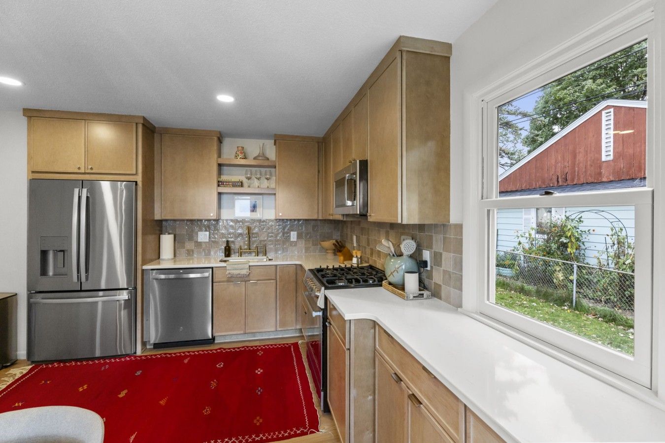 A modern kitchen with stainless steel appliances, wooden cabinets, and a red rug.