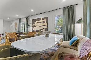 Uma sala de estar moderna com área de jantar, apresentando uma grande pintura abstrata, uma mesa redonda e assentos confortáveis.