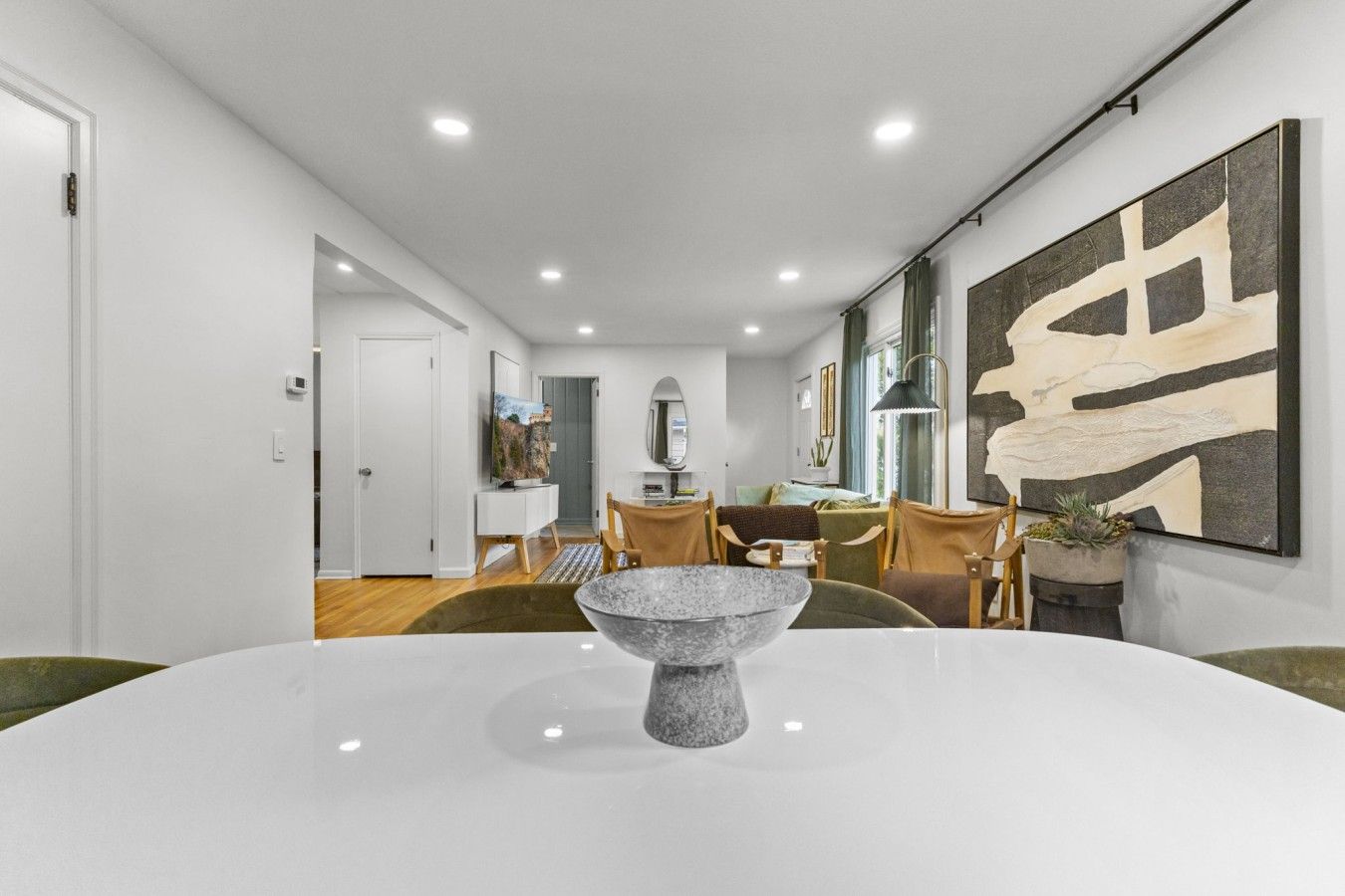Un espace repas moderne avec une table blanche, des chaises et un grand vase décoratif placé au centre.