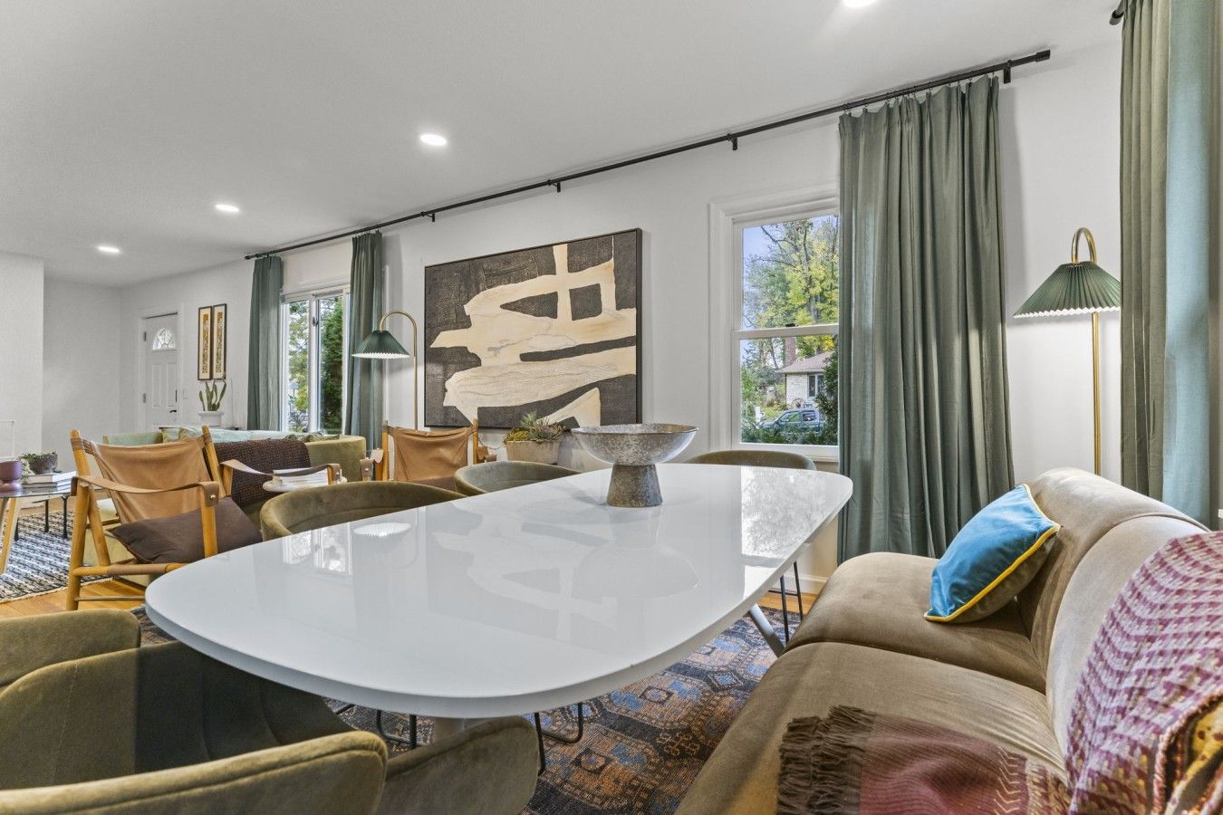 Uma sala de estar moderna com área de jantar, apresentando uma grande pintura abstrata, uma mesa redonda e assentos confortáveis.