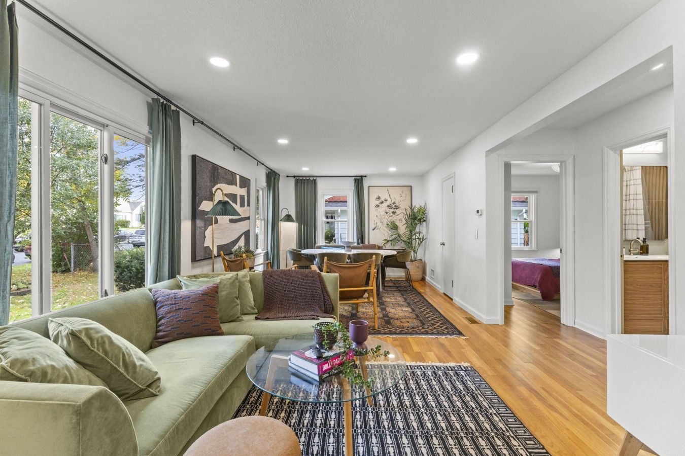 Uma sala de estar moderna com um sofá verde, uma mesa de centro de vidro e um espaço de jantar com mesa e cadeiras.