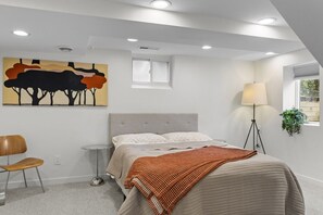 Quarto com cama, cadeira, abajur e um quadro na parede.