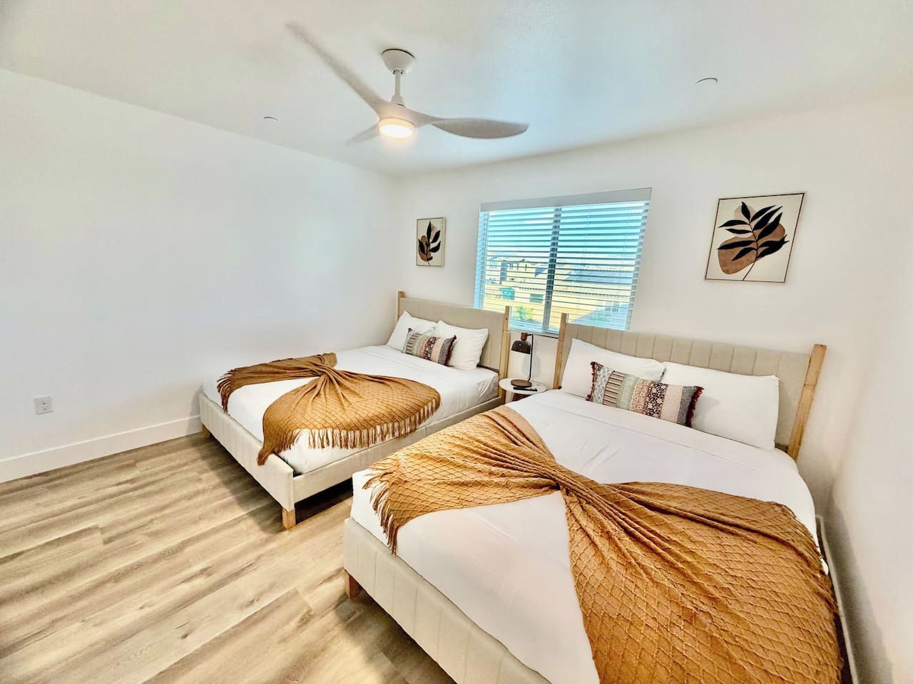 A hotel room with two beds, a ceiling fan, and a window with blinds.