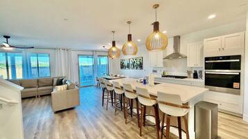 A modern kitchen with a central island, bar stools, and a dining area with a sofa.