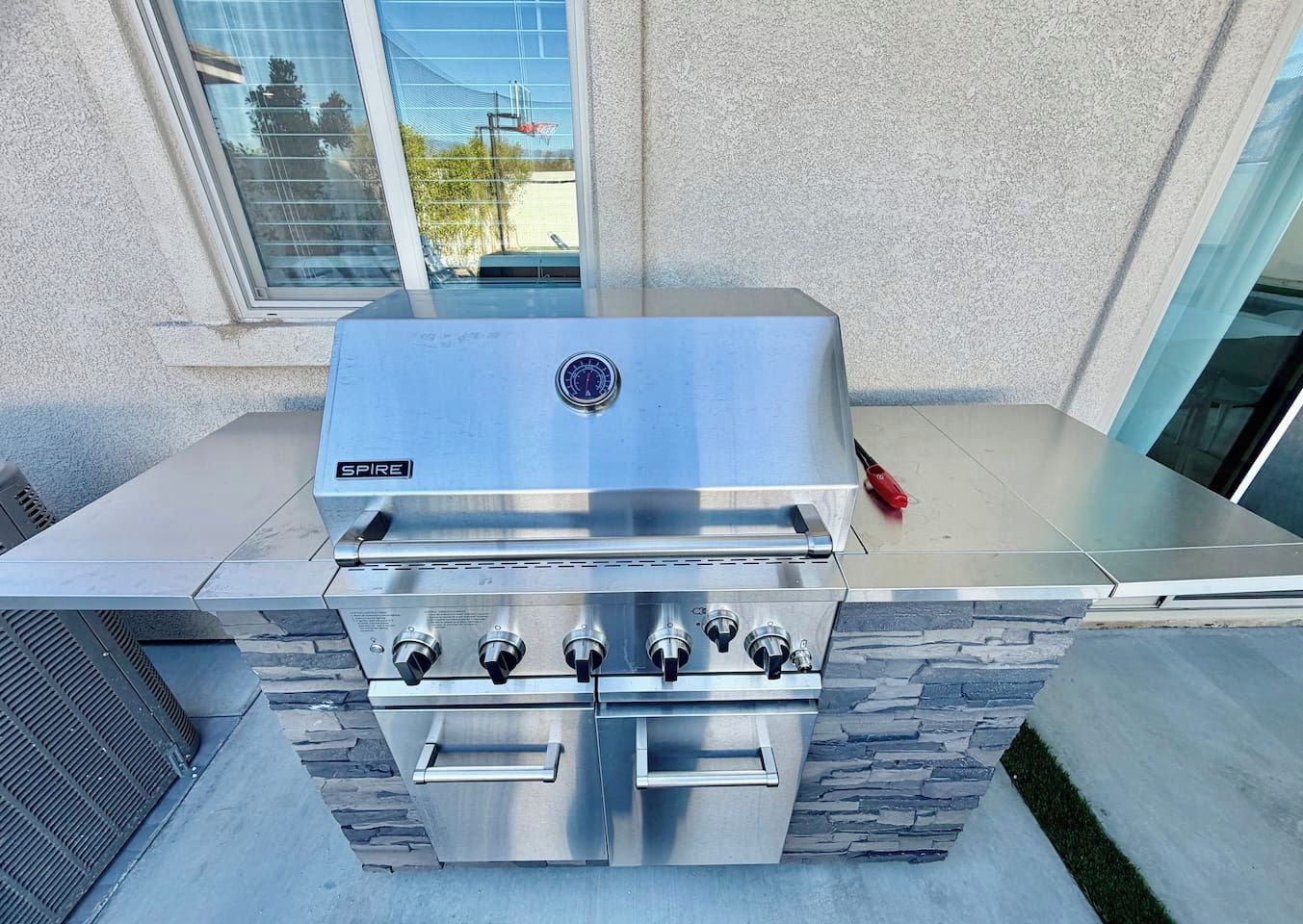 A stainless steel outdoor kitchen with a built-in grill, a control panel, and a stone accent wall.