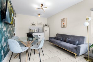 A modern living room with a glass dining table, grey sofa, and a kitchen area with a microwave and coffee maker. - Byronessa Miami Beach (Miami Beach)