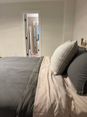 Un lit avec une couette grise et blanche, une tête de lit en bois et une vue sur une pièce avec une porte et des rideaux.