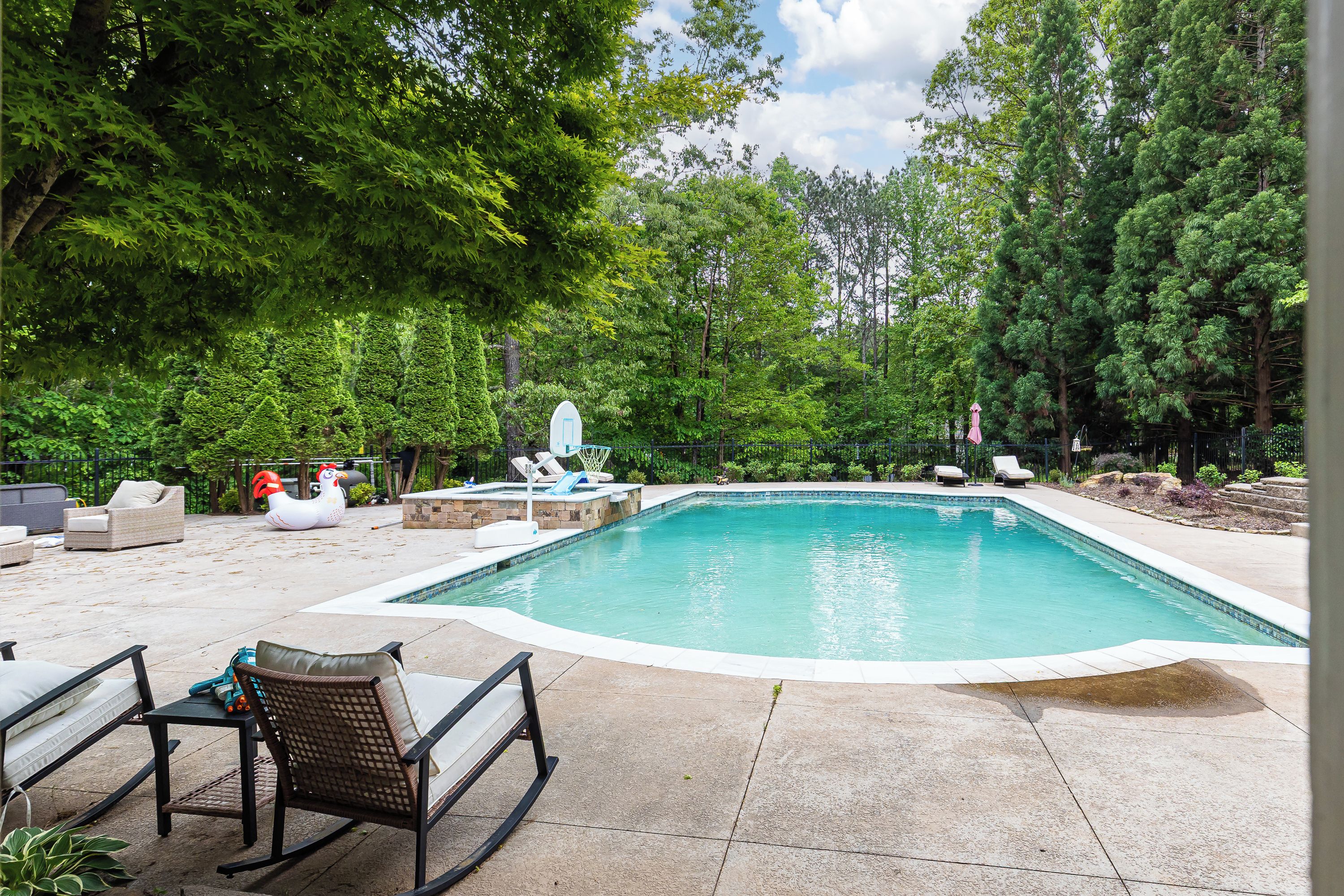 A swimming pool with lounge chairs and a bird-shaped float, surrounded by trees.