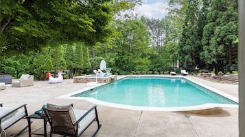 A swimming pool with lounge chairs and a bird-shaped float, surrounded by trees.