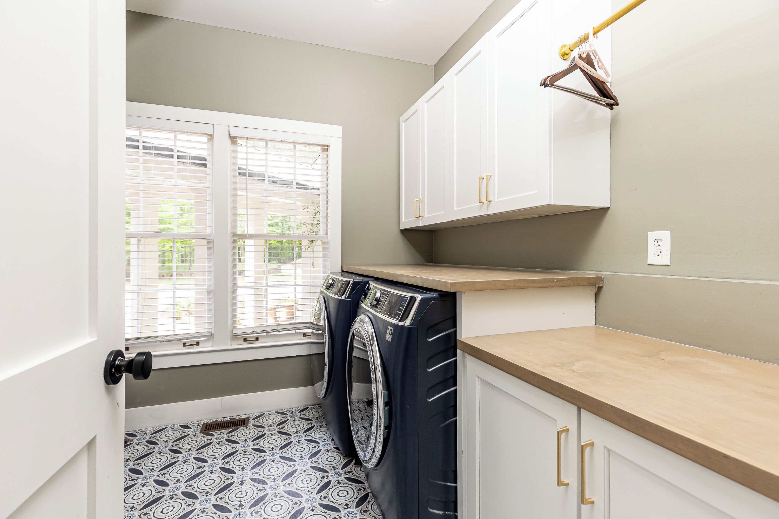 A laundry room with a washing machine, a drying rack, and a window with blinds.