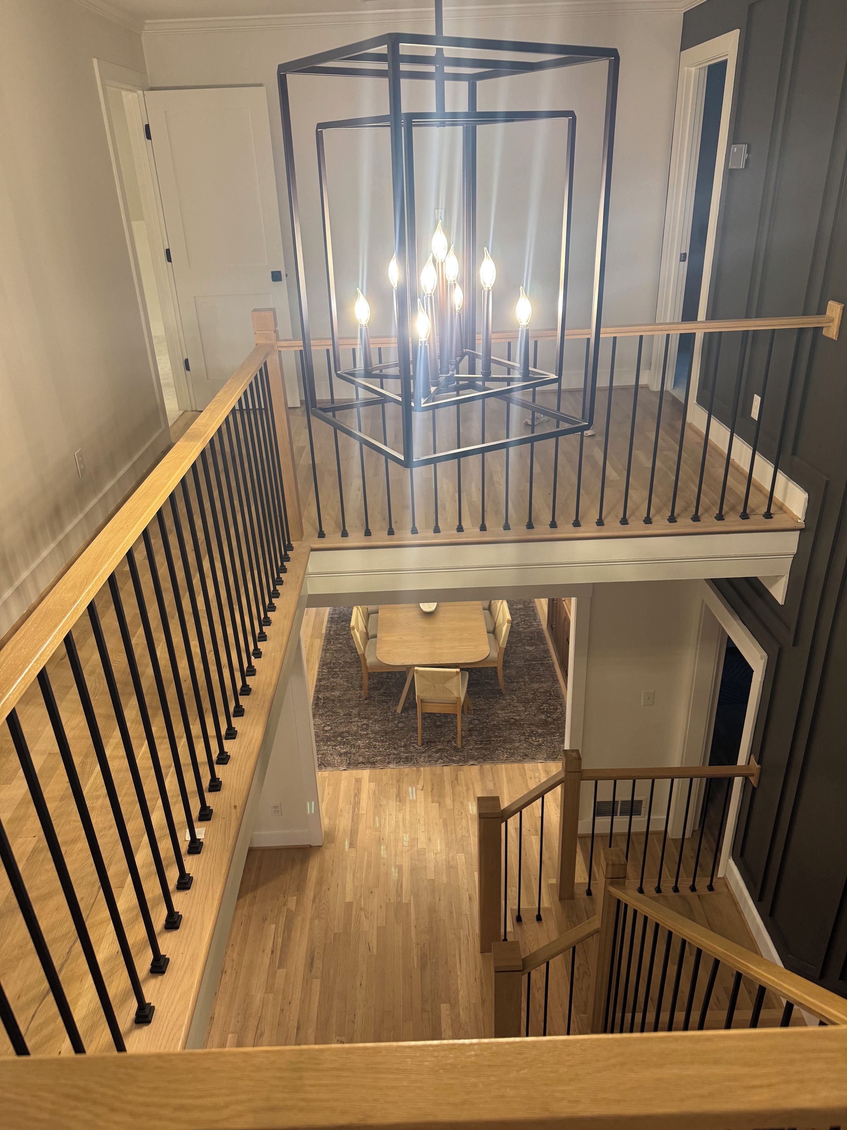 A multi-level interior with a wooden staircase, a dining area with a table and chairs, and a modern chandelier.
