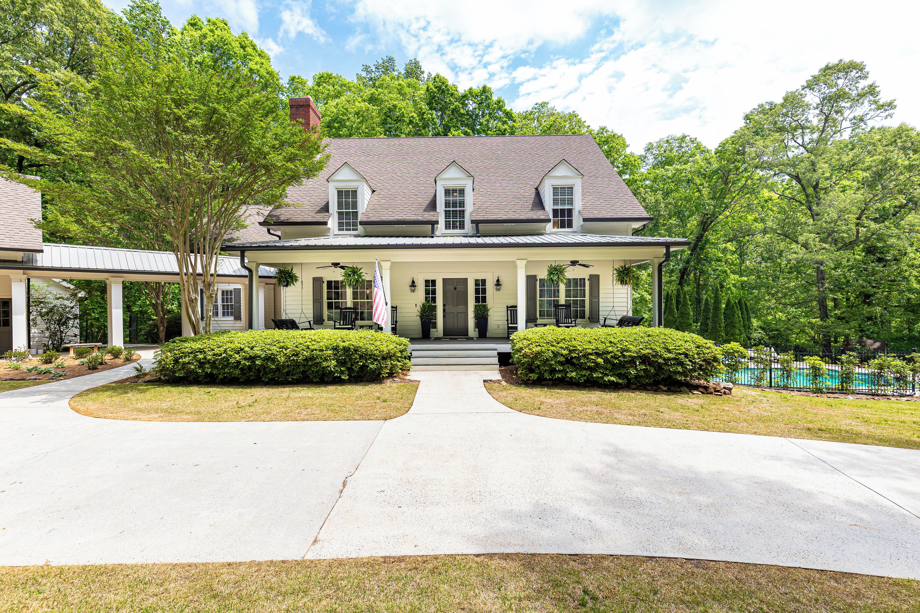 A two-story house with a front porch, a driveway, and a swimming pool in the background.