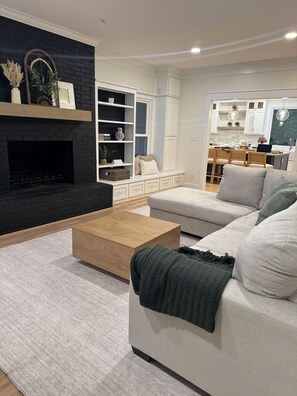A modern living room with a fireplace, a sofa, a coffee table, and a kitchen area in the background. - Dream home in Acworth - Pool and close to Lakepoint (Acworth)