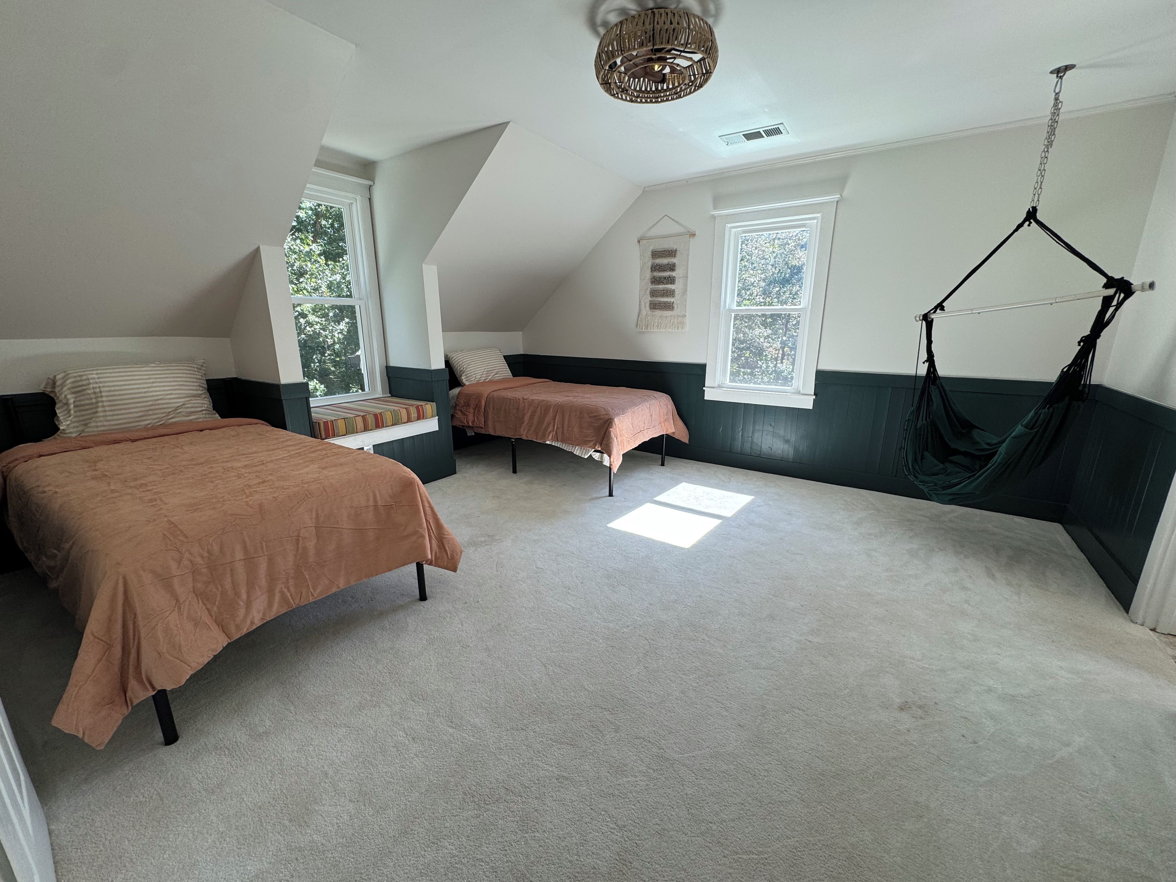 A bedroom with two beds, a window, a hanging chair, and a ceiling fan.