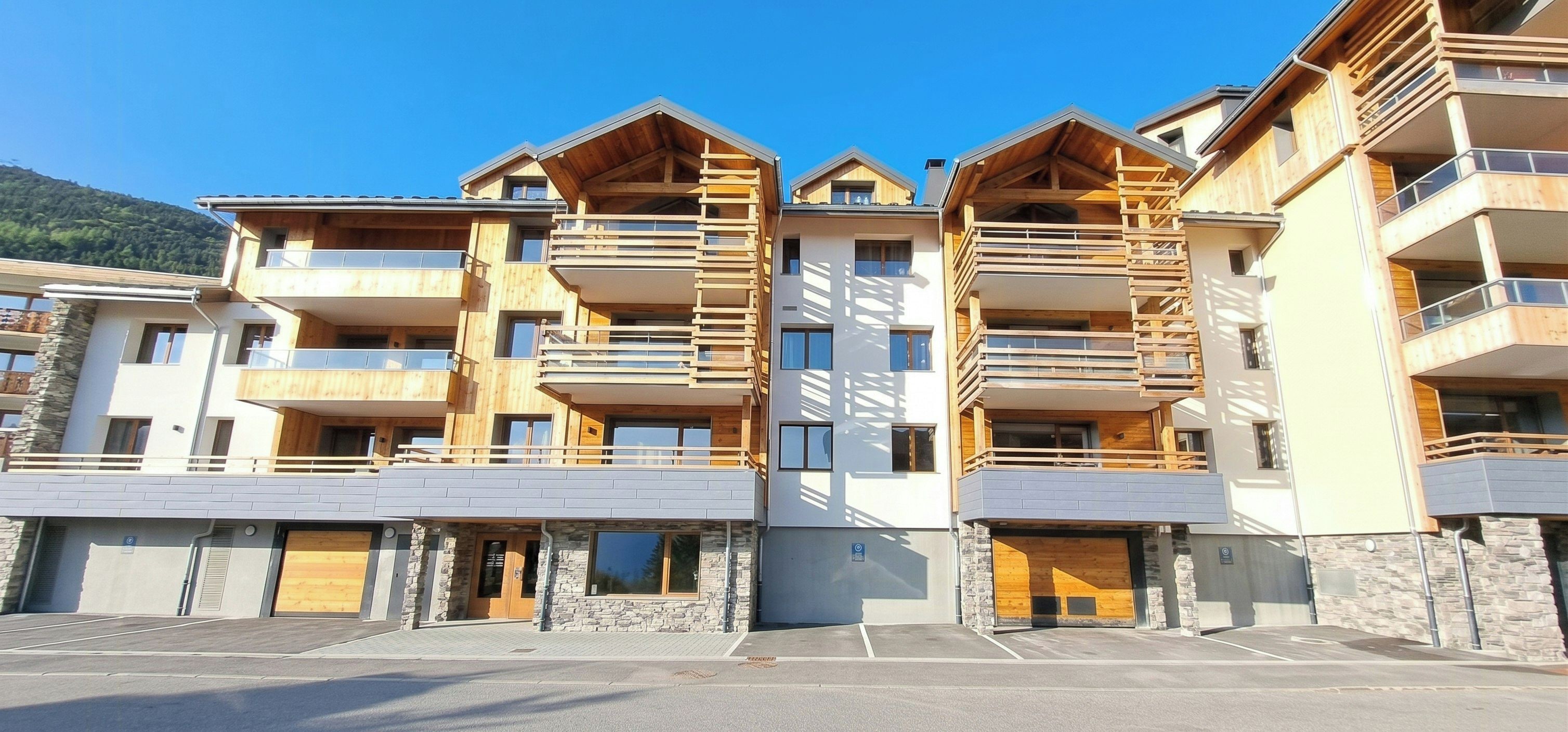 A multi-story hotel with balconies, a parking area, and a mountain backdrop.