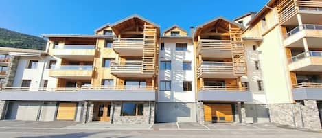 A multi-story hotel with balconies, a parking area, and a mountain backdrop.