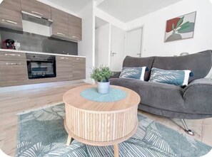 A modern living space with a kitchen, a grey sofa, and a round wooden coffee table with a plant.