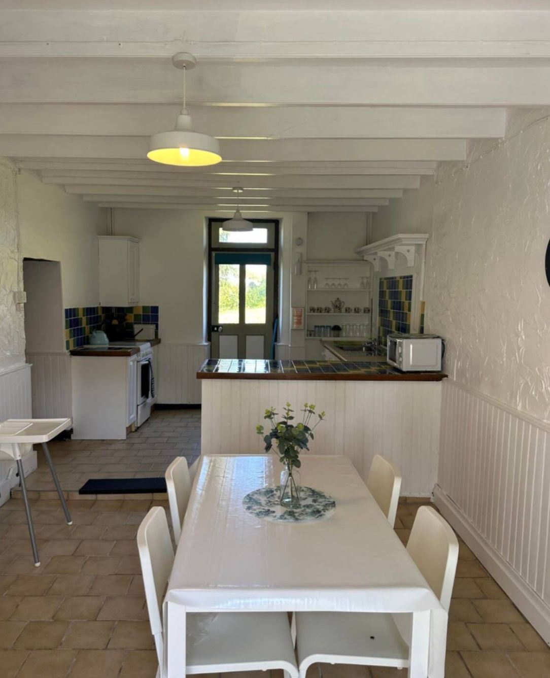 A dining area with a table and chairs, a kitchen in the background, and a door leading outside.