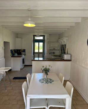 En matplats med ett bord och stolar, ett kök i bakgrunden och en dörr som leder ut.