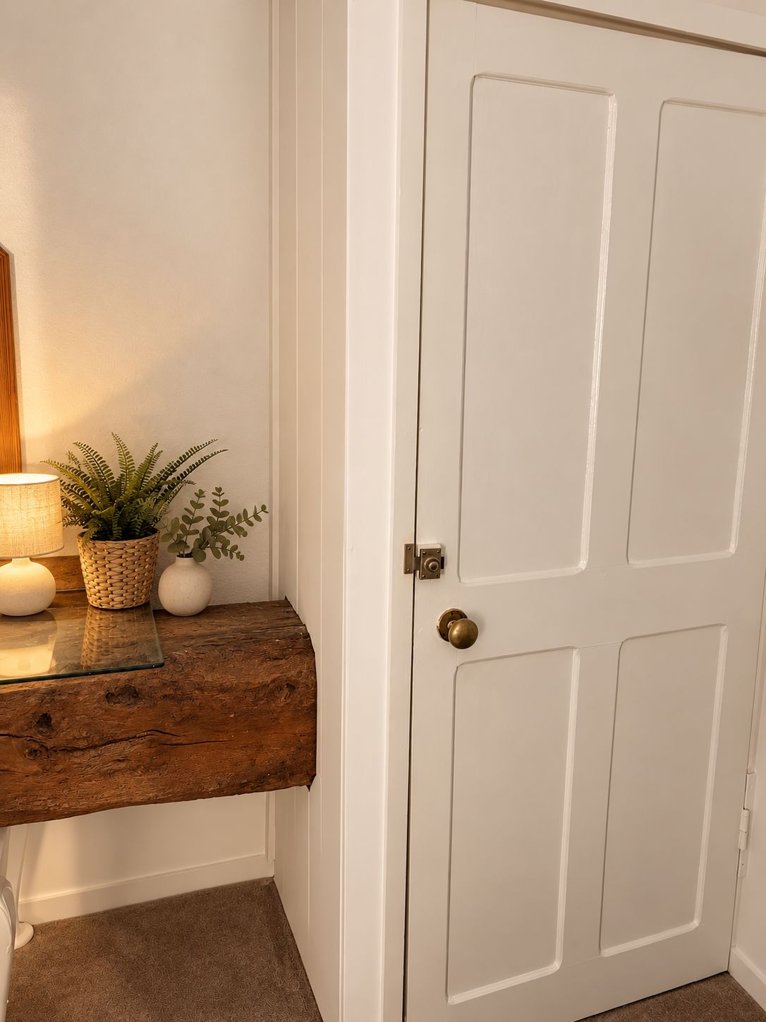 A white door with a brass doorknob, a wooden bench with a woven basket and potted plants, and a wall-mounted lamp.